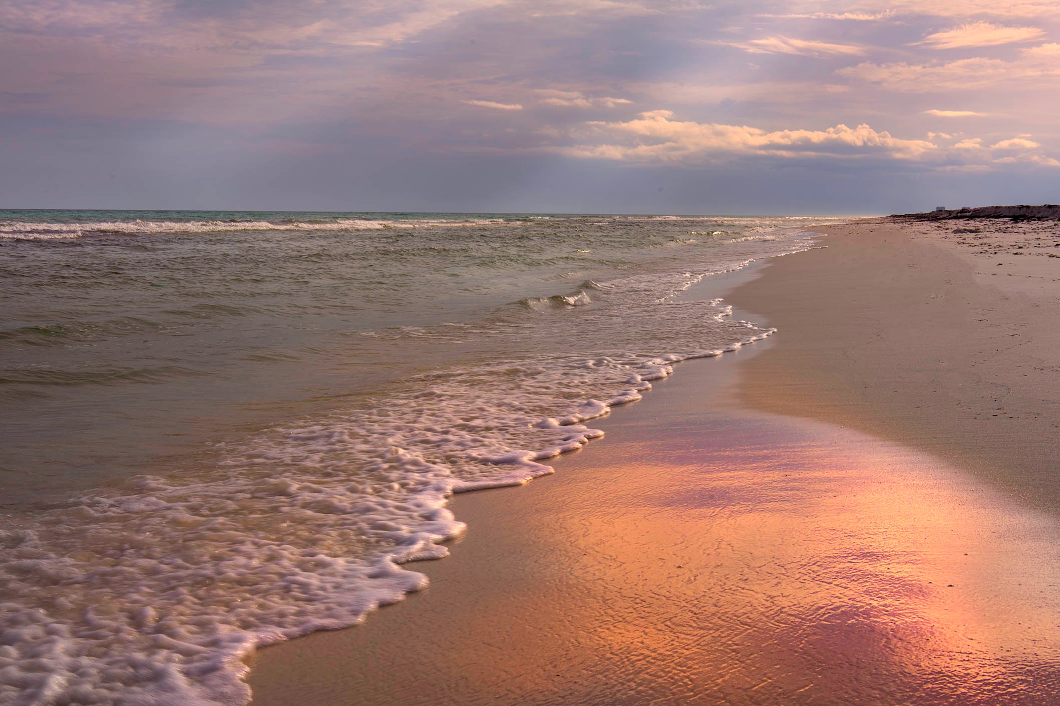 Soft pink and lavender sunset light reflected in the wet sand at the water's edge