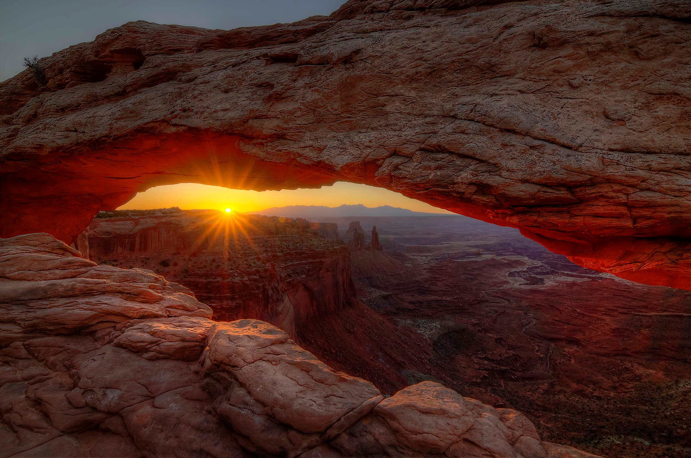 Sunrise flooding through a sandstone arch in the Utah canyon lands, warm amber light on ancient rock