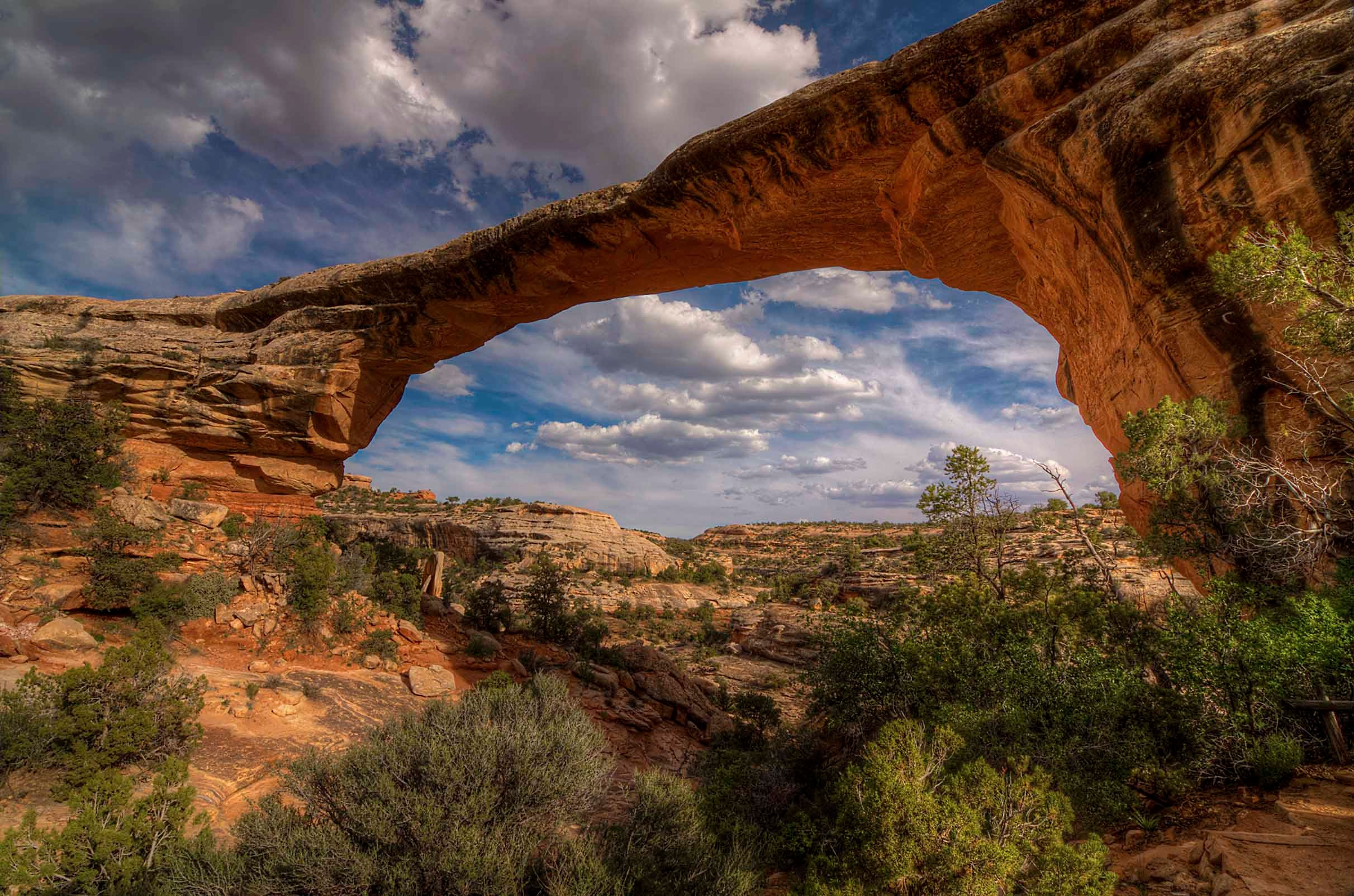 A massive natural sandstone arch spanning the Utah sky, red rock framing a view of canyon country and billowing clouds beyond