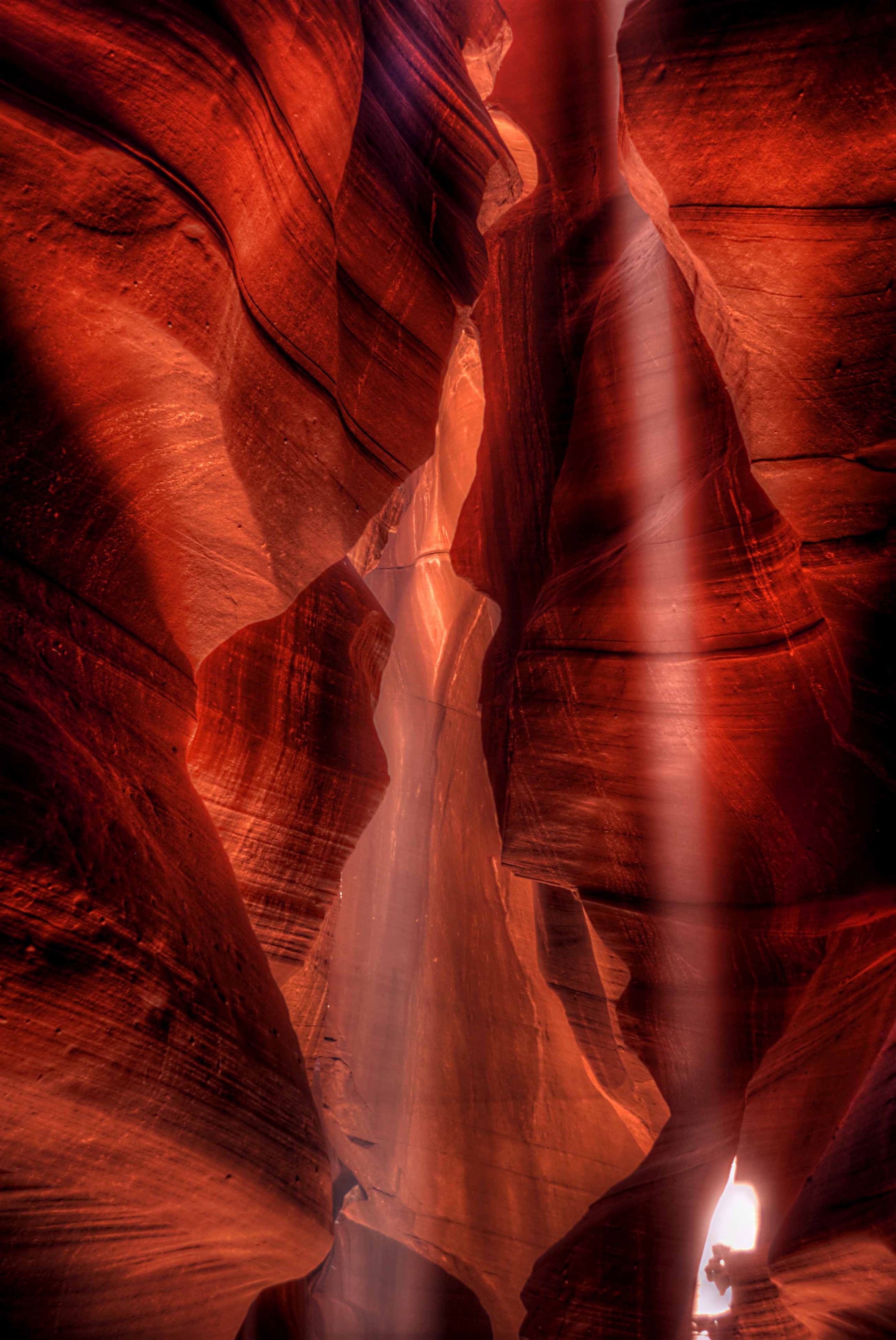 A single beam of light descending through the crimson walls of Upper Antelope Canyon, illuminating the sandy floor in a pool of white light