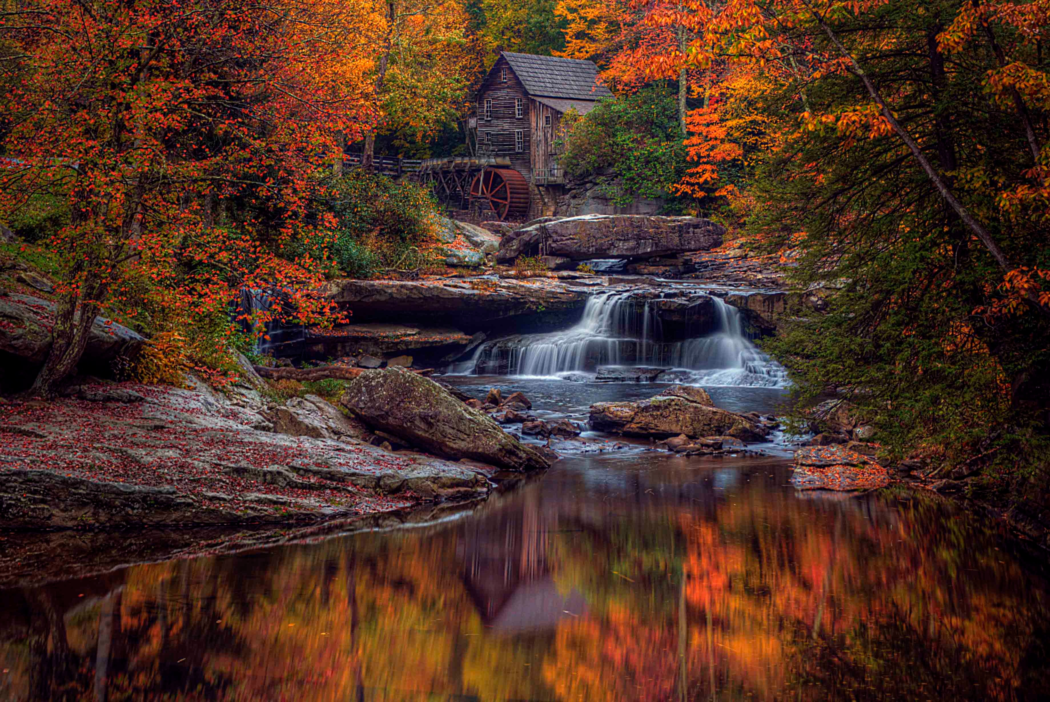 Historic grist mill with water wheel surrounded by blazing autumn foliage reflected in a still river pool, West Virginia