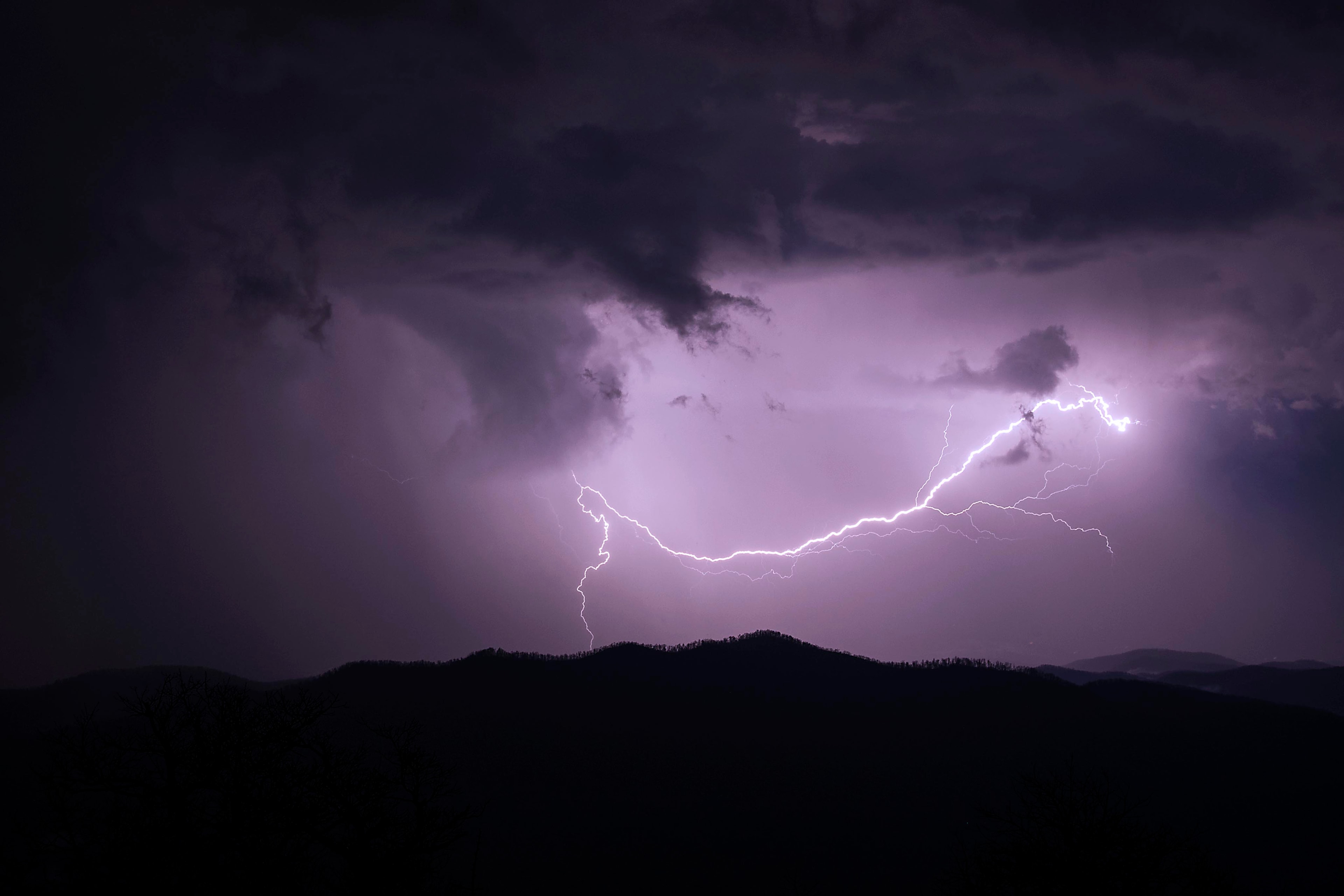 A vivid purple lightning bolt arcing across the sky above the silhouetted Blue Ridge Mountains at night